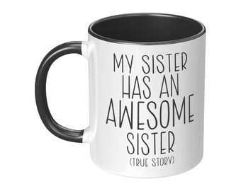 May include: White ceramic coffee mug with a black interior and handle. The mug has black text that reads "My sister has an awesome sister (true story)".