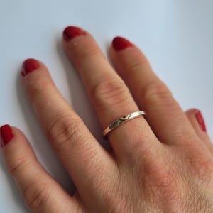 May include: A silver ring with a small gold heart design on the band.