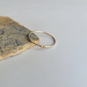 May include: A simple silver band ring with a small gold bead accent.