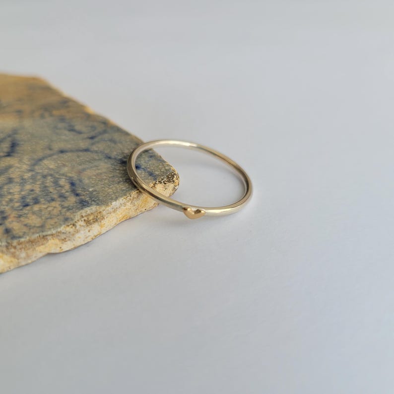 May include: A simple silver band ring with a small gold bead accent.