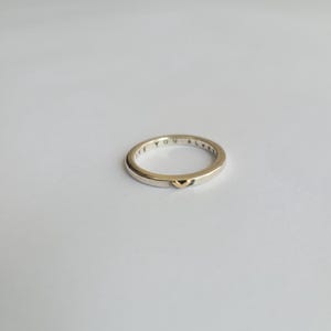 May include: A silver band ring with the words "Love You Always" engraved on the outside and a small gold heart on the inside.