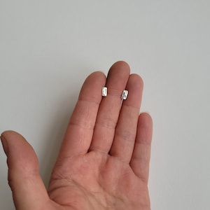 May include: A pair of silver rectangle shaped stud earrings. The earrings are small and have a hammered texture.