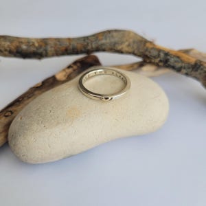 May include: A gold band ring inscribed with the words "If you always" on the outside of the band. The ring is resting on a light brown stone.