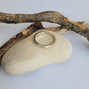 May include: A silver ring with the inscription "YOU ALWAYS" engraved on the band. The ring is resting on a light brown rock.