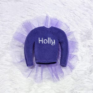 May include: Purple elf sweater with a tulle skirt and the name "Holly" embroidered on the front.