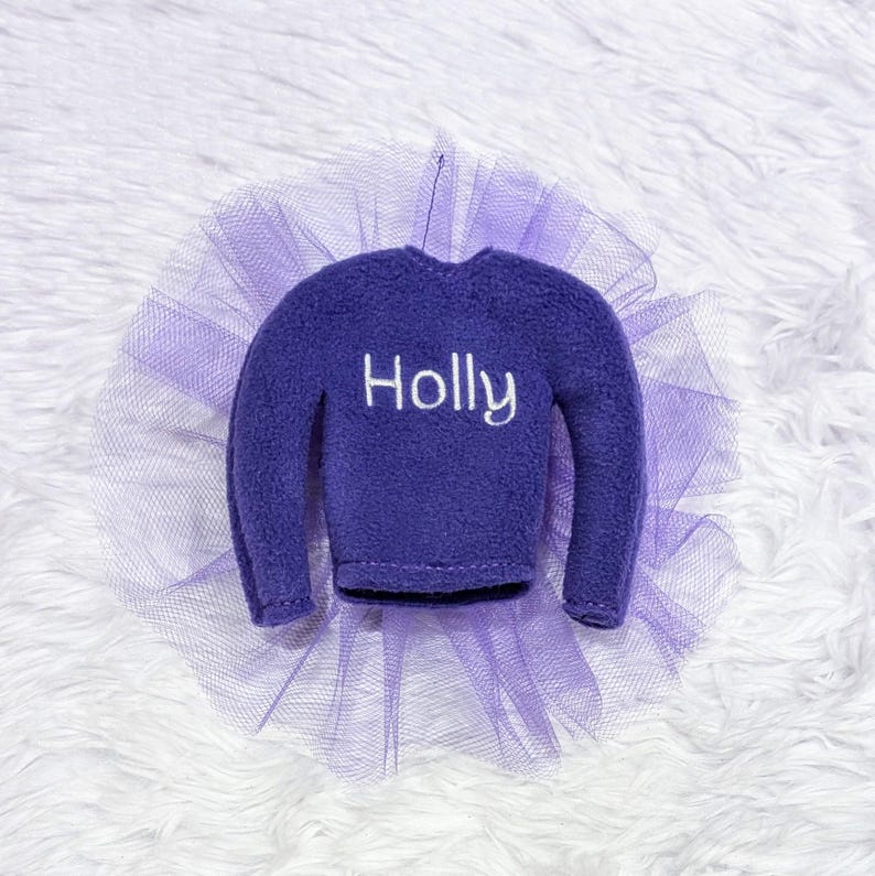 May include: Purple elf sweater with a tulle skirt and the name "Holly" embroidered on the front.