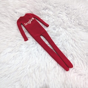 May include: A red doll with long legs and arms, with the word "Jingles" in white script across the chest. The doll is lying on a white, fluffy surface.