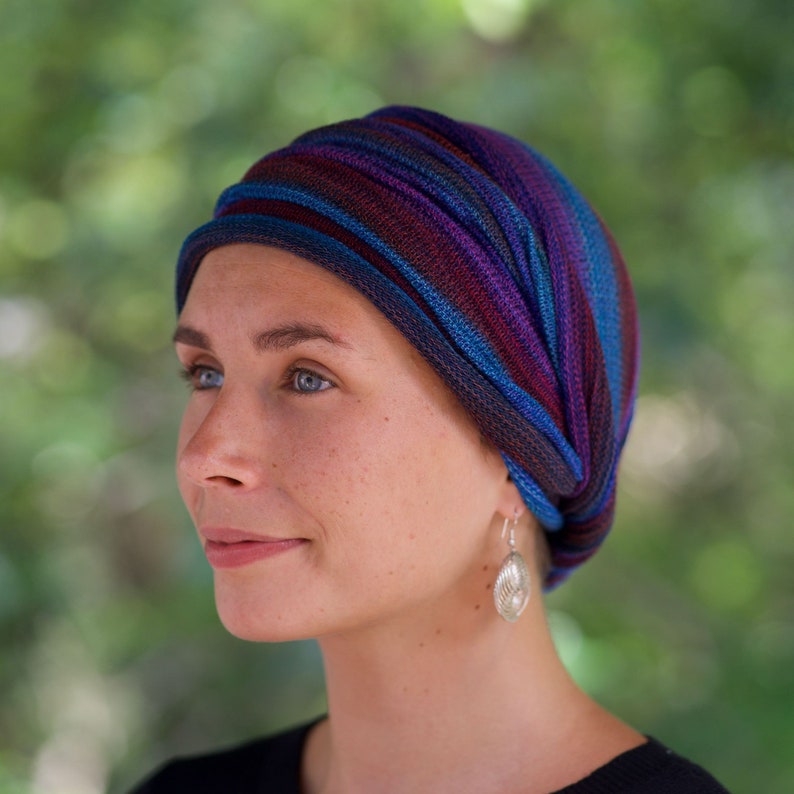Puede incluir: Una mujer con un turbante a rayas azul, morado y rojo con un pendiente de plata. El turbante est&aacute; atado en un nudo en la parte posterior de su cabeza.