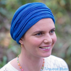 Op de afbeelding: Een vrouw draagt een blauwe turban. De turban is gemaakt van een zachte, textuurrijke stof. De vrouw glimlacht en kijkt naar rechts. De tekst "Turquoise Blues" is zichtbaar in de rechterbenedenhoek van de afbeelding.