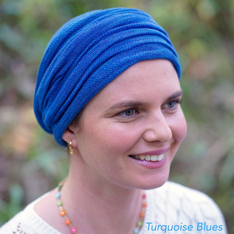 Op de afbeelding: Een vrouw draagt een blauwe turban. De turban is gemaakt van een zachte, textuurrijke stof. De vrouw glimlacht en kijkt naar rechts. De tekst "Turquoise Blues" is zichtbaar in de rechterbenedenhoek van de afbeelding.
