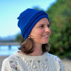 Pu&ograve; includere: Una donna indossa un berretto blu brillante e un maglione color crema con ricami floreali. Il berretto &egrave; di un colore blu brillante e uniforme. Il maglione ha un design a trecce con delicati dettagli floreali.