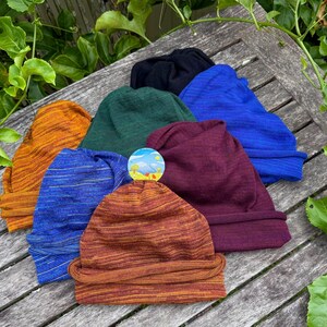 Pu&ograve; includere: Una collezione di sette berretti in vari colori, tra cui arancione, verde, blu, nero e bordeaux. I berretti sono realizzati in un tessuto strutturato e sono disposti su una superficie di legno.