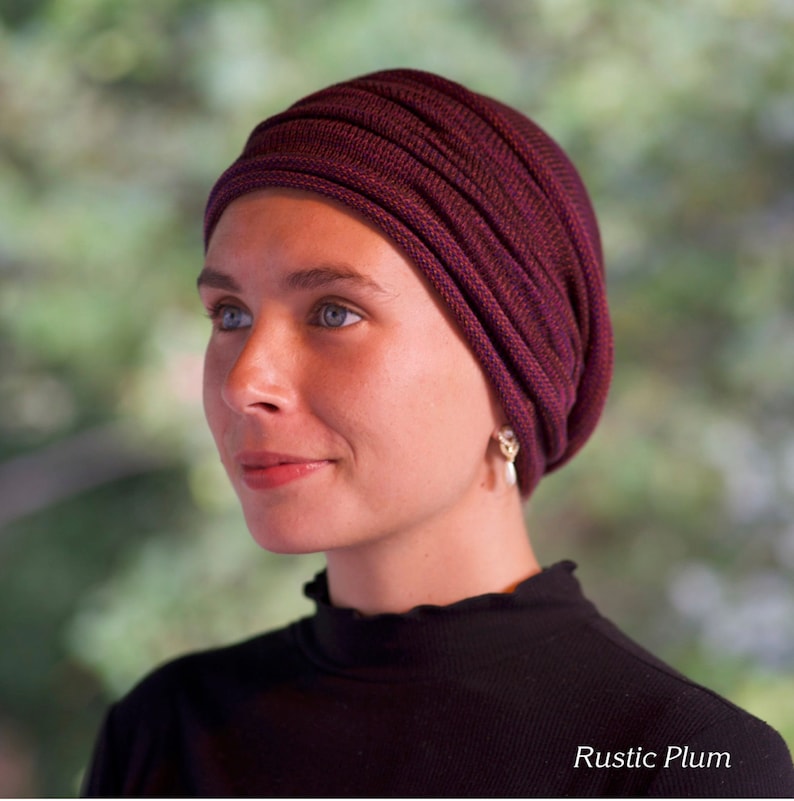 Puede incluir: Una mujer lleva una gorra de punto de color morado oscuro con nervaduras y una camisa negra de cuello alto. La gorra se llama "Rustic Plum".