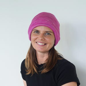 Pu&ograve; includere: Un berretto a righe rosa e bianche. Il cappello &egrave; realizzato in un morbido materiale a maglia. Il cappello &egrave; indossato da una persona con lunghi capelli castani e una maglietta nera.