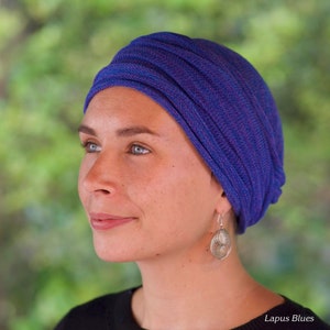 Op de afbeelding: Een vrouw draagt een blauwe en paarse turban met zilveren oorbellen. De turban is gemaakt van een zachte, rekbare stof en is ontworpen om comfortabel en stijlvol te zijn.