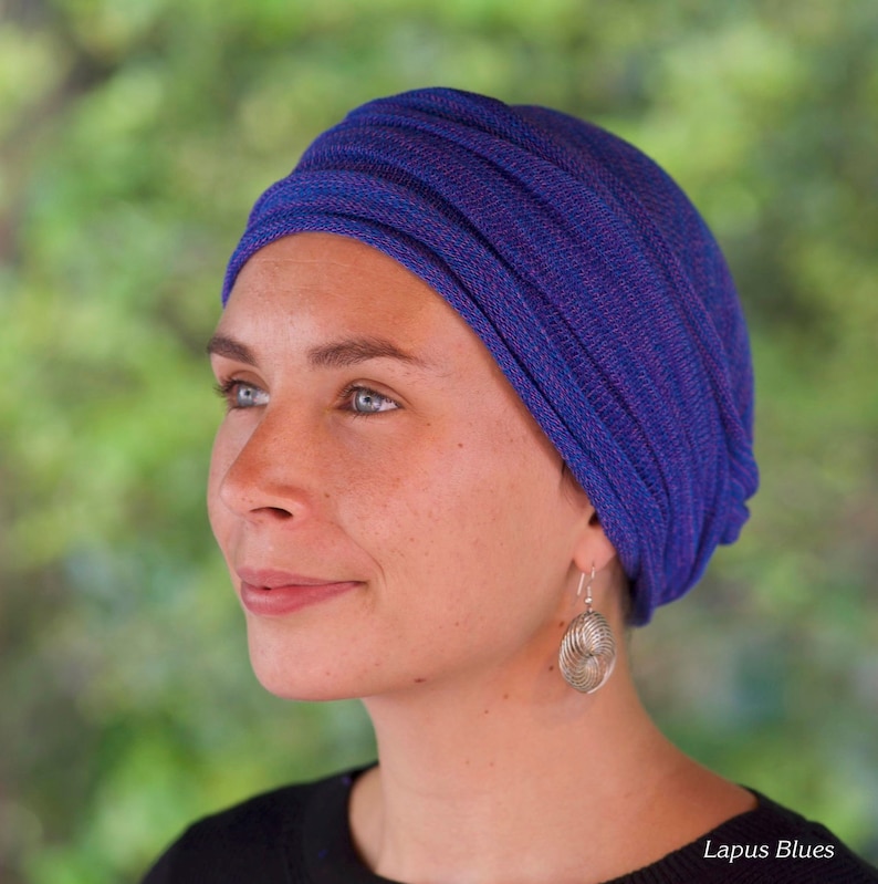 Op de afbeelding: Een vrouw draagt een blauwe en paarse turban met zilveren oorbellen. De turban is gemaakt van een zachte, rekbare stof en is ontworpen om comfortabel en stijlvol te zijn.
