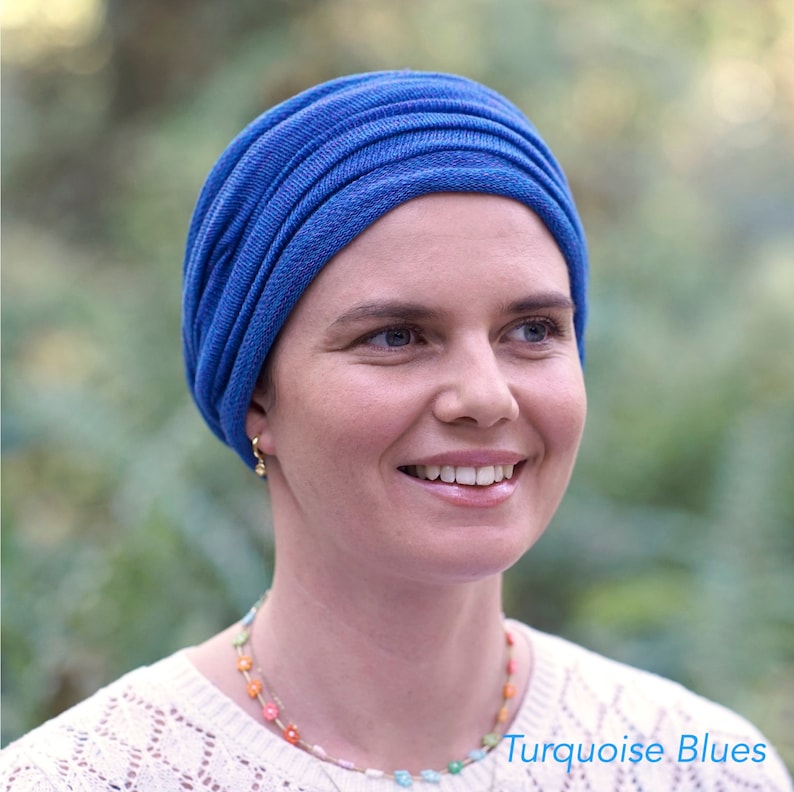 Op de afbeelding: Een vrouw draagt een blauwe tulband met een witte gehaakte trui en een kleurrijke kralenketting. De tekst "Turquoise Blues" is zichtbaar in de rechterbenedenhoek van de afbeelding.