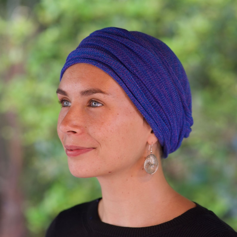 Op de afbeelding: Een vrouw draagt een blauwe en paarse turban met een zilveren oorring. De turban is gemaakt van een zachte, rekbare stof en is ontworpen om comfortabel en stijlvol te zijn.