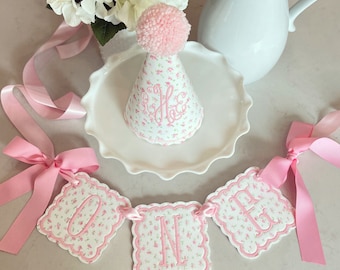 Una pancarta para trona con bordado floral rosa de Rosie y un sombrero de fiesta con monograma. Decoración para el primer cumpleaños. Piezas individuales disponibles.