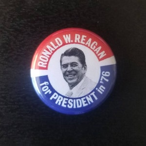 Puede incluir: Un botón rojo, blanco y azul con una imagen de Ronald W. Reagan y el texto "Ronald W. Reagan for President in '76".
