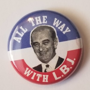 Puede incluir: Un botón rojo, blanco y azul con una foto en blanco y negro de Lyndon B. Johnson. El botón dice "All the Way with L.B.J."