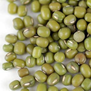 May include: A close-up view of a pile of green mung beans. The beans are small and round, with a slightly wrinkled surface.