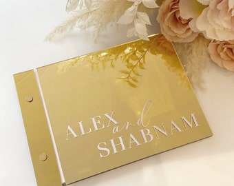 May include: Gold mirror guest book with white text that reads "ALEX and SHABNAM".