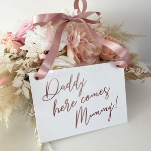 May include: White sign with a pink ribbon attached. The sign says "Daddy here comes Mummy!" in rose gold lettering.