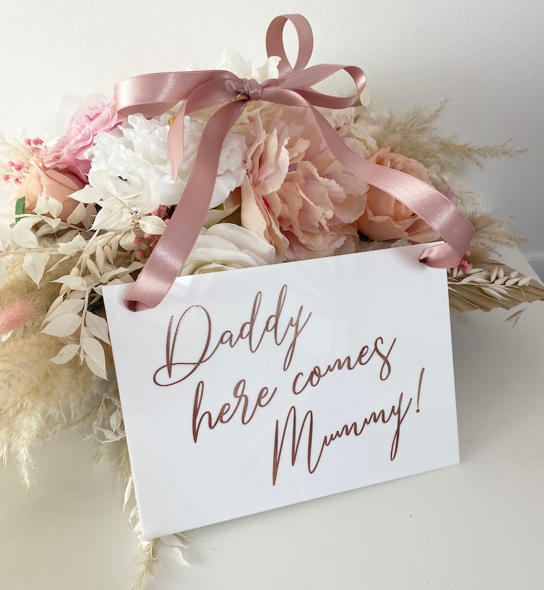 May include: White sign with a pink ribbon attached. The sign says "Daddy here comes Mummy!" in rose gold lettering.