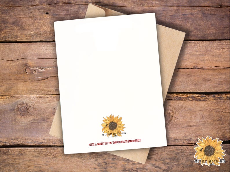 May include: A blank white greeting card with a sunflower illustration and a kraft paper envelope. The card features the text "THE BURBS AND THE BEES" and a website address. The card is set against a rustic wooden background.