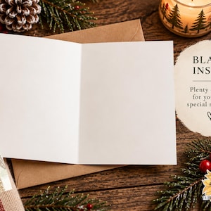 May include: An open greeting card with a blank white interior, resting on a brown envelope. The card features a partial illustration of a figure in a winter hat on the front cover. Text on the right reads: BLANK INSIDE, Plenty of room for your own special message.