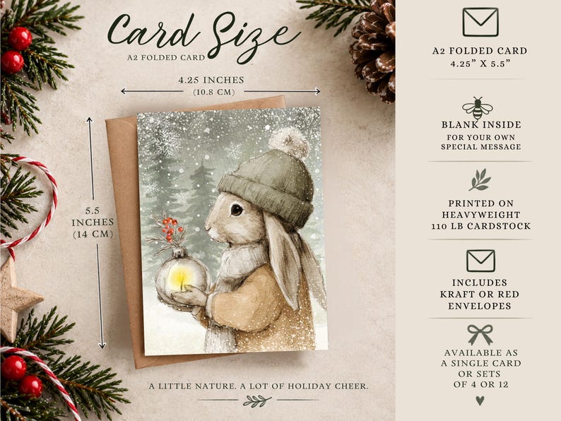 May include: An A2 folded card measuring 4.25 by 5.5 inches, featuring a watercolor illustration of a rabbit in a winter hat holding a glowing ornament. The card is printed on 110 lb cardstock, includes a kraft or red envelope, and is blank inside.