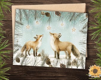 May include: A watercolour illustration of two foxes looking up at star decorations. The foxes are set in a winter scene with pine needles, snow, and pine cones. The artwork is on a greeting card.
