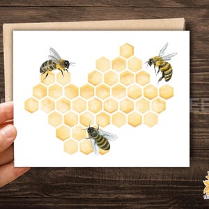 May include: A greeting card featuring a watercolor illustration of three bees and a honeycomb. The bees are yellow and black, and the honeycomb is a light yellow. The card is on a white background.
