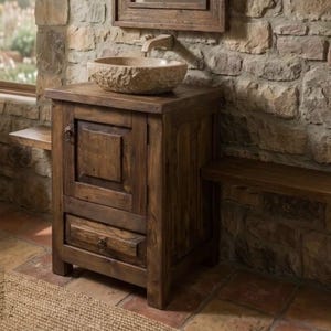 May include: A dark brown wooden vanity cabinet featuring a single door with a square recessed panel, a bottom drawer with a metal ring pull, and a light-colored, rough-textured stone vessel sink mounted on top with a matching metal faucet.