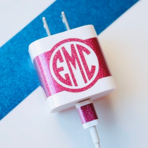 Może przedstawiać: Biała ładowarka do telefonu z różową błyszczącą naklejką z monogramem, na której widnieje napis "EMC".