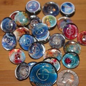 May include: A collection of colorful glass cabochons with a compass design and the text "Geocaching the Universe".