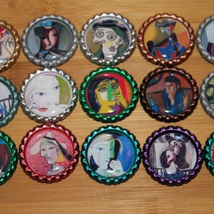 Könnte beinhalten: Eine Sammlung von fünfzehn Flaschendeckeln, die jeweils ein anderes künstlerisches Design aufweisen. Die Kappen haben eine Vielzahl von Metallic-Farben, darunter Gold, Silber und Grün. Die Kunstwerke auf den Kappen scheinen vom Stil Picassos inspiriert zu sein.