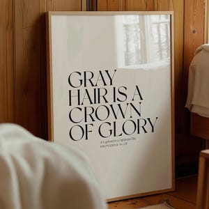 May include: A framed print with the text "GRAY HAIR IS A CROWN OF GLORY" in black, with the scripture reference Proverbs 16:31. The print has a light-colored background and a wooden frame. The image is set in a bedroom.