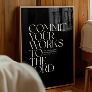 Puede incluir: Un estampado en blanco y negro enmarcado con el texto "COMMIT YOUR WORKS TO THE LORD" en una fuente serif. El estampado también incluye el texto "And your thoughts will be established. PROVERBS 16:3". El marco es de color marrón claro.