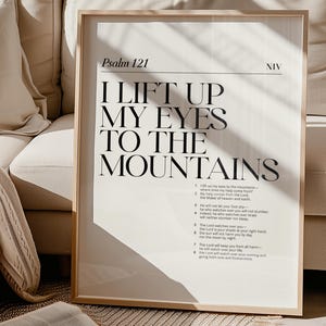 以下が含まれることがあります： 白い背景に黒い文字で書かれた額装されたプリント。テキストには「私は山に向かって目を上げる」とあり、NIV 翻訳の詩篇 121 が含まれています。