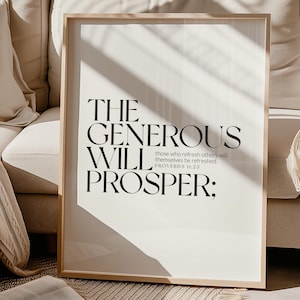 May include: A framed print with the text "THE GENEROUS WILL PROSPER:" in black, with the Bible verse Proverbs 11:25. The print is in a light wood frame and is displayed on a beige sofa. An open book rests on a woven rug.