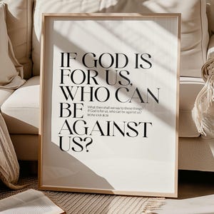 Op de afbeelding: Een ingelijste print met de tekst "IF GOD IS FOR US, WHO CAN BE AGAINST US?" in een vetgedrukte, zwarte letter. De print zit in een licht houten frame en wordt weergegeven tegen een neutrale achtergrond. Een open boek ligt op de voorgrond.