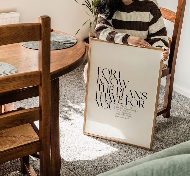 May include: A beige poster with a black and white quote that reads "FOR I KNOW THE PLANS I HAVE FOR YOU" and a smaller quote from Jeremiah 29:11. The poster is framed in a thin, gold frame.