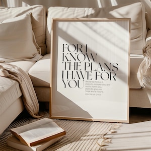 May include: A black and white inspirational quote print with the text "For I know the plans I have for you" and the scripture reference "Jeremiah 29:11". The print is framed in a light wood frame and is sitting on a white couch.