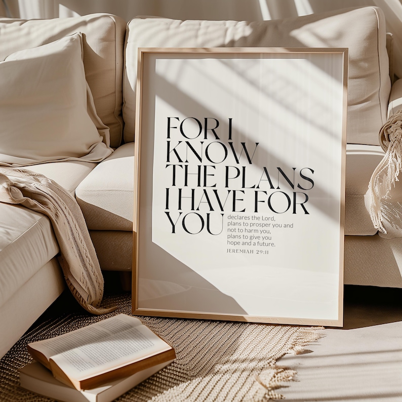 May include: A black and white inspirational quote print with the text "For I know the plans I have for you" and the scripture reference "Jeremiah 29:11". The print is framed in a light wood frame and is sitting on a white couch.