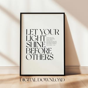 May include: Black framed print with the text "LET YOUR LIGHT SHINE BEFORE OTHERS" in a bold, elegant font. The words "DIGITAL DOWNLOAD" are at the bottom. The print is displayed on a light-colored wall and wooden floor.