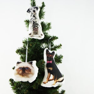 Peut inclure: Un sapin de No&euml;l d&eacute;cor&eacute; de trois ornements sur le th&egrave;me des animaux de compagnie. Les ornements repr&eacute;sentent un dalmatien, un chat Ragdoll et un berger allemand portant des lunettes et un n&oelig;ud papillon. Chaque ornement est blanc avec une image d'animal.