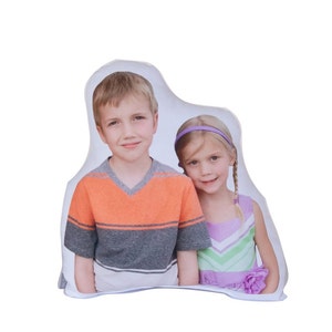 May include: A white pillow featuring a photograph of two children, a boy and a girl, smiling at the camera. The boy is wearing an orange and grey striped shirt and the girl is wearing a purple and green dress.