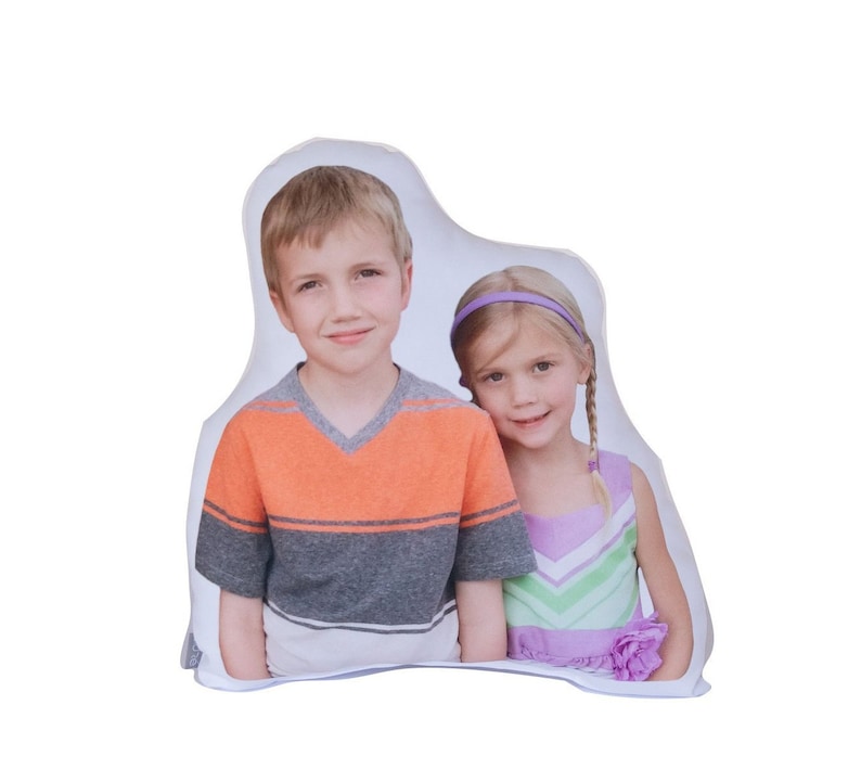 May include: A white pillow featuring a photograph of two children, a boy and a girl, smiling at the camera. The boy is wearing an orange and grey striped shirt and the girl is wearing a purple and green dress.
